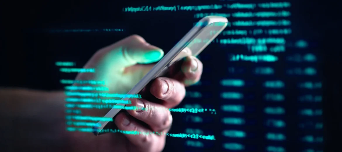 Käsi pitelee puhelinta, taustalla koodia