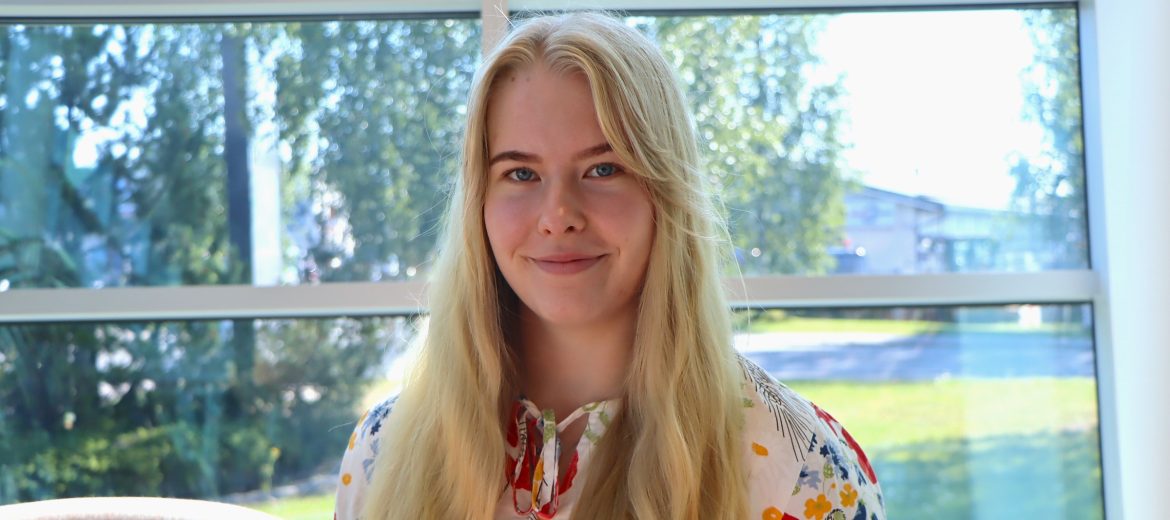 Puolikuva viestintäharjoittelija Jenna Ala-Rantalasta Vesitalon ikkunoita vasten