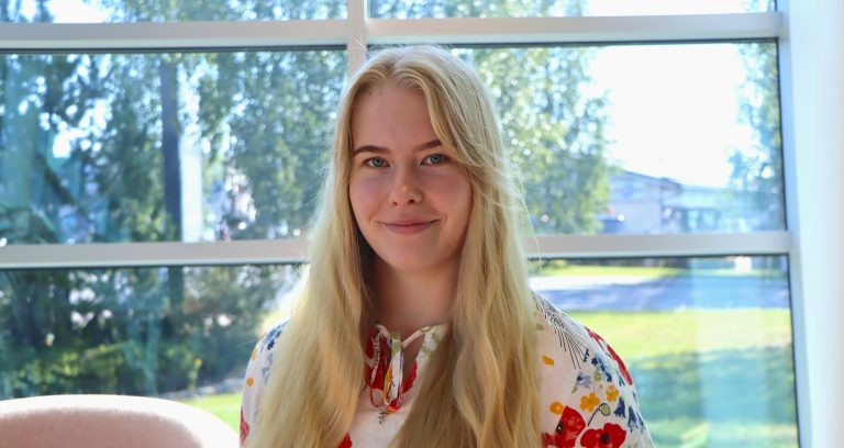 Puolikuva viestintäharjoittelija Jenna Ala-Rantalasta Vesitalon ikkunoita vasten